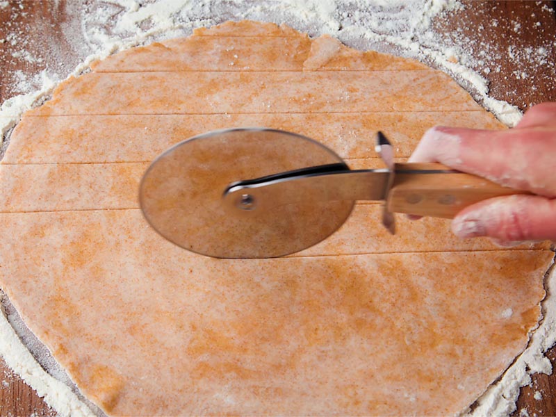 rolled vegan pie dough being cut with a pizza cutter