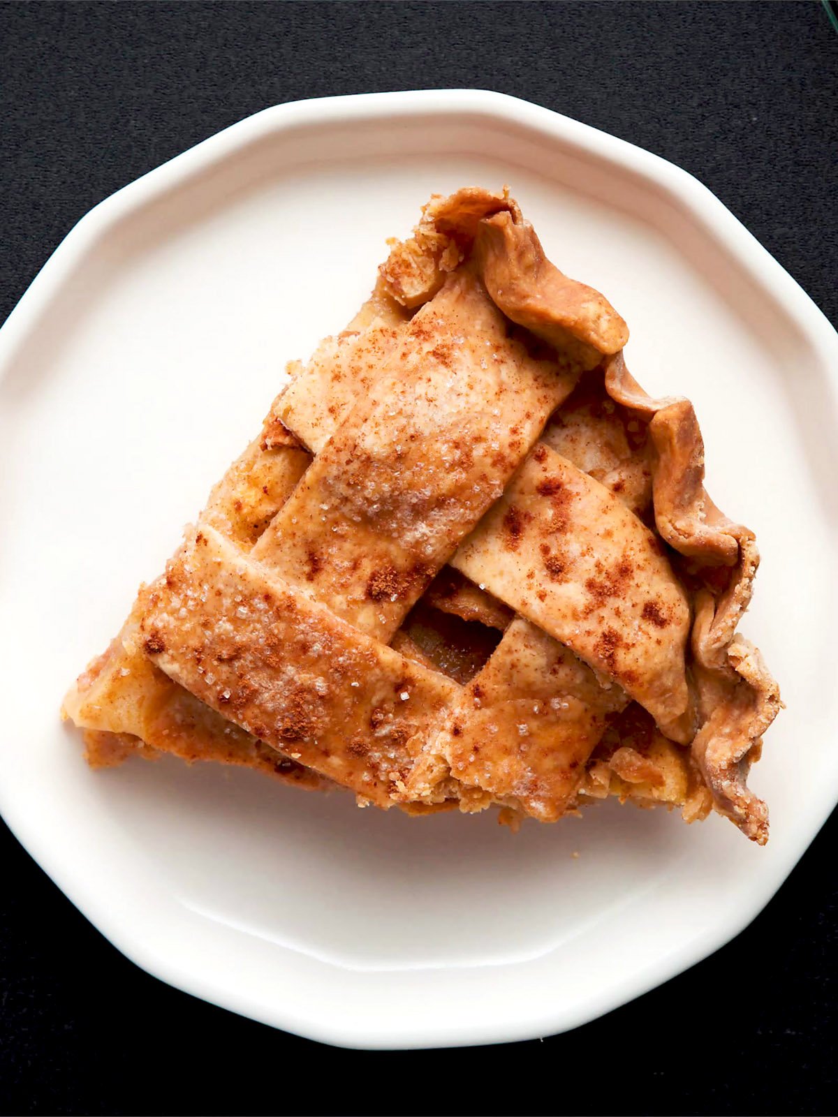 a triangular wedge of apple pie on an off-white plate