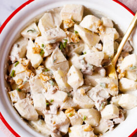 Apple salad with celery, walnuts and mayo dressing in an enamel bowl with white interior and red exterior with a brass spoon