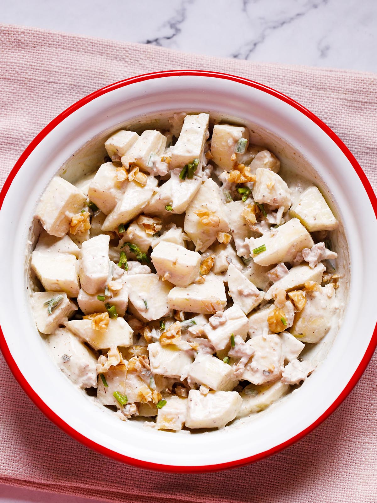 Apple salad with walnuts, celery and mayo dressing in an enamel bowl with white interior and red exterior