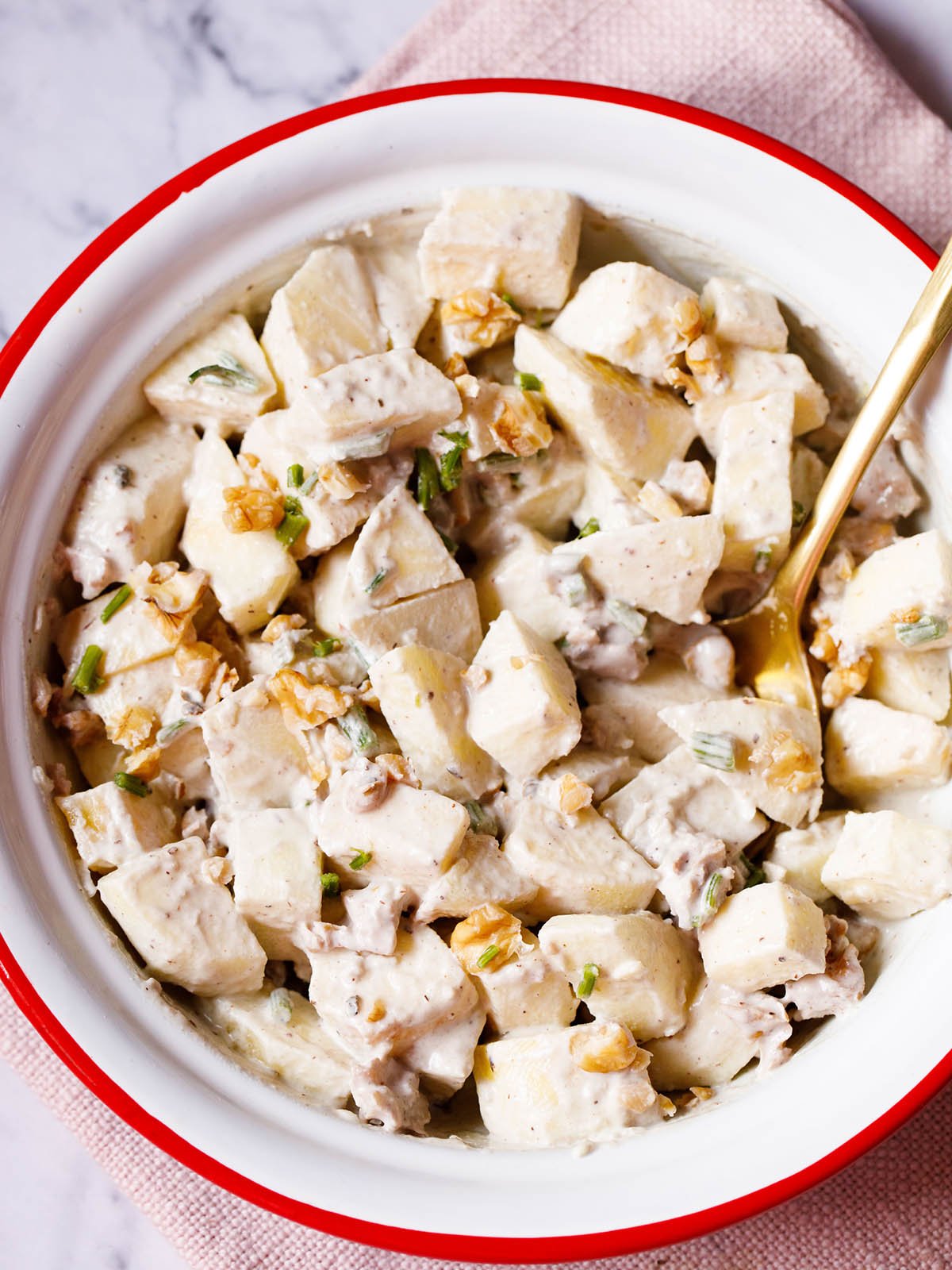 Apple salad with celery, walnuts and mayo dressing in an enamel bowl with white interior and red exterior with a brass spoon