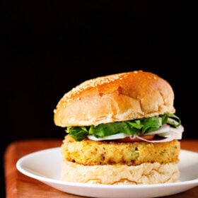 veggie burger on a white plate on wooden board with a black backdrop