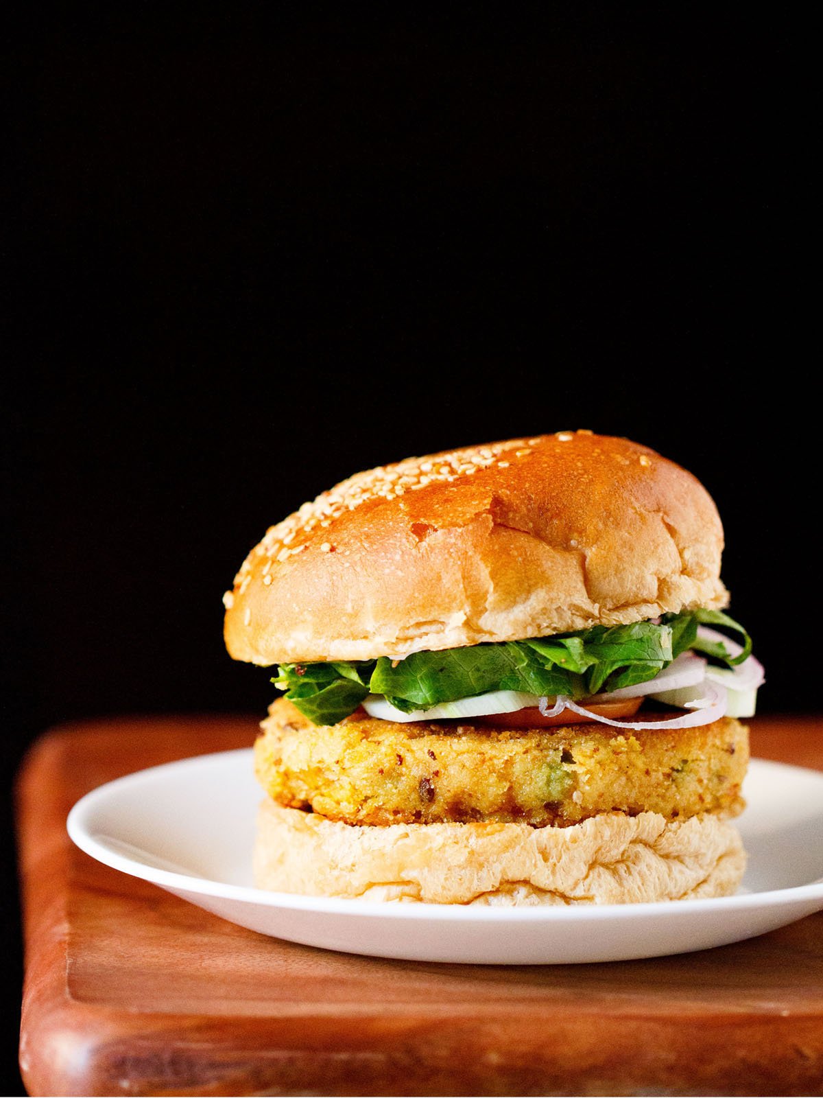 veggie burger on a white plate on wooden board with a black backdrop