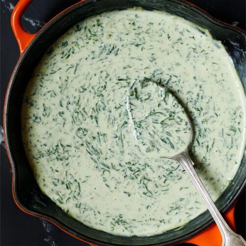 Creamed spinach in a skillet with a brass spoon inside