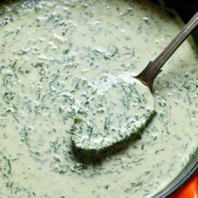 creamed spinach in a skillet with a brass spoon inside