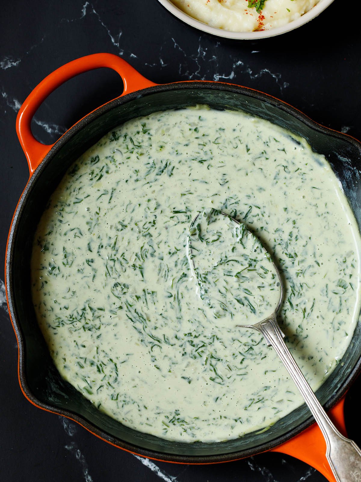 overhead shot of completed creamed spinach in the skillet with a side dish of mashed potatoes on a black background