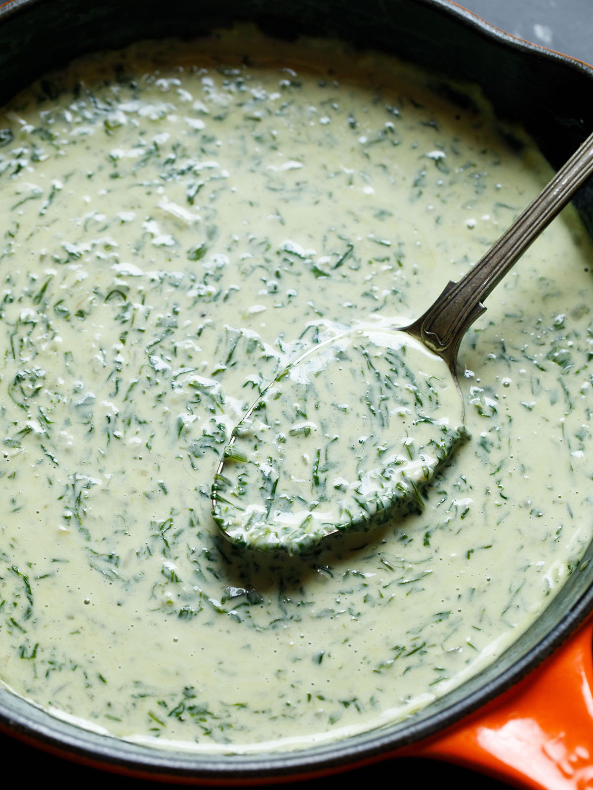 creamed spinach in a skillet with a brass spoon inside