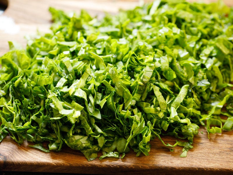 fresh spinach leaves cut into ribbons on a wood cutting board