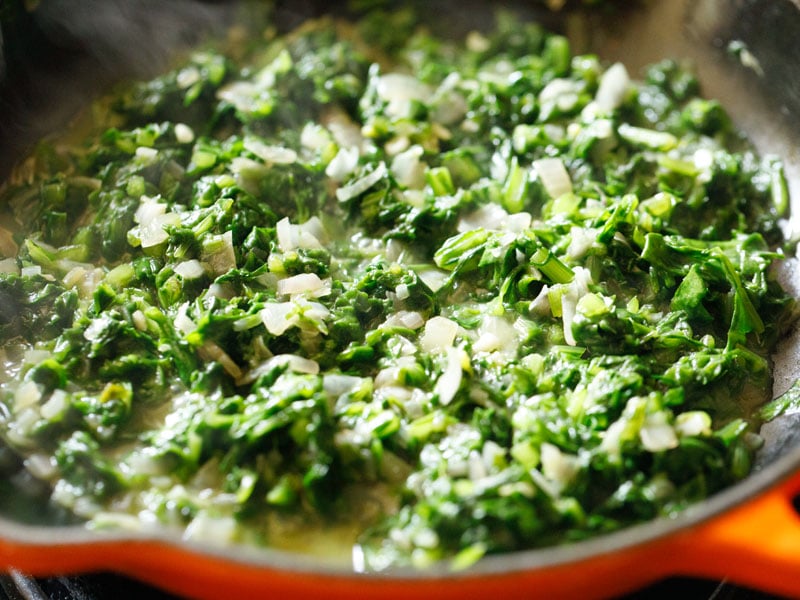 spinach and onion mixture after wilting down in a red/orange enameled cast iron