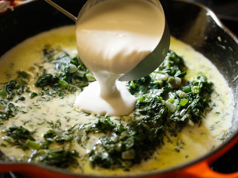 cream being poured into spinach mixture and milk filled skillet