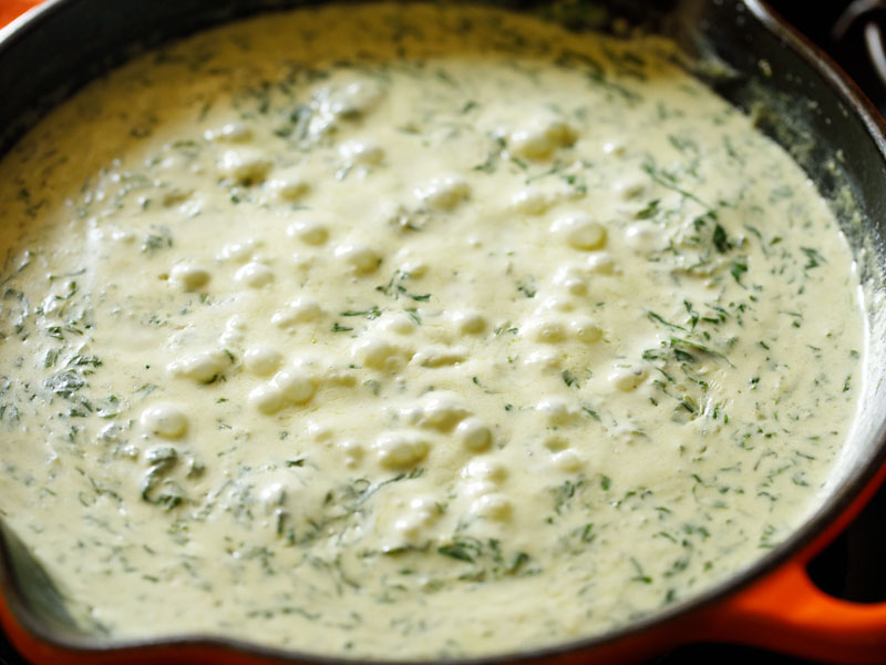 cream sauce is beginning to bubble in the skillet with the spinach