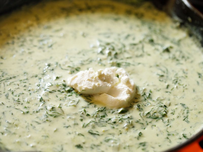 dollop of cream cheese on top of cooked spinach and cream sauce