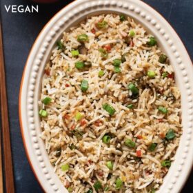 veg fried rice in an oval ceramic bowl with wooden chopsticks on a slate black board