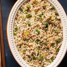 fried rice in a oval ceramic bowl with wooden chopsticks at side on a slate black board