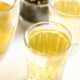 green tea in a transparent glass with a glass mug sideways on a white marble board