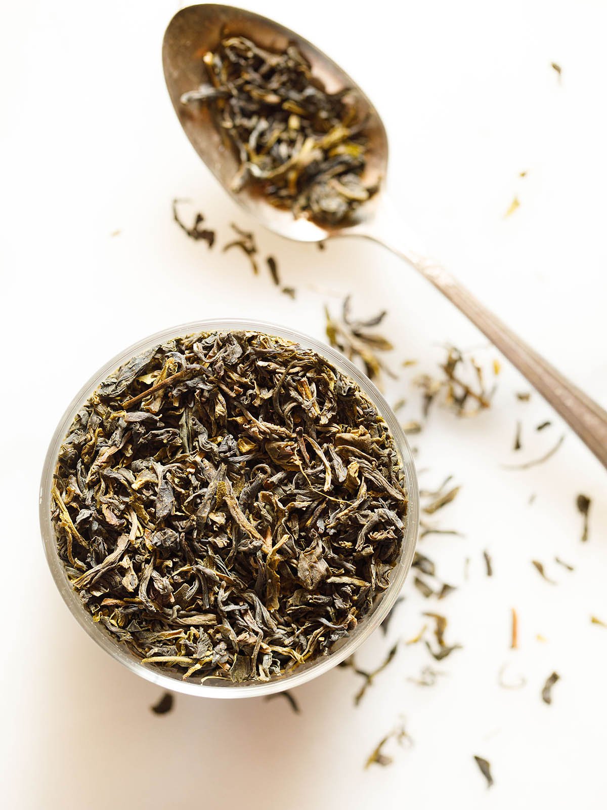 green tea leaves in a bowl and on a silver spoon on a white marble background