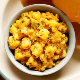 jeera aloo served in a ceramic bowl with a side of puri