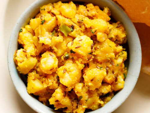 jeera aloo served in a ceramic bowl with a side of puri