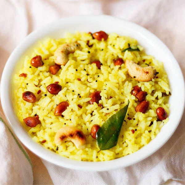 yellow colored lemon rice served in a white bowl on a white cotton cloth