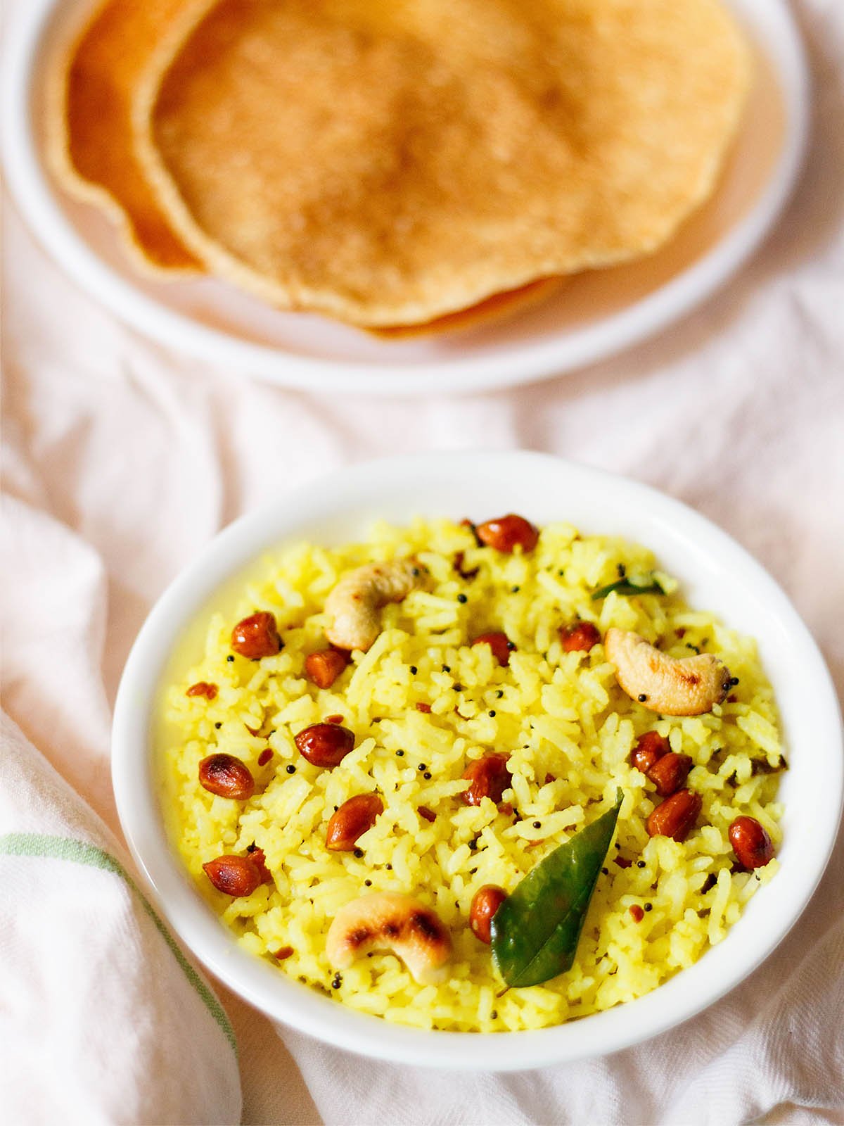 lemon rice served in a white bowl on a white cotton cloth with a side of fried papaddums