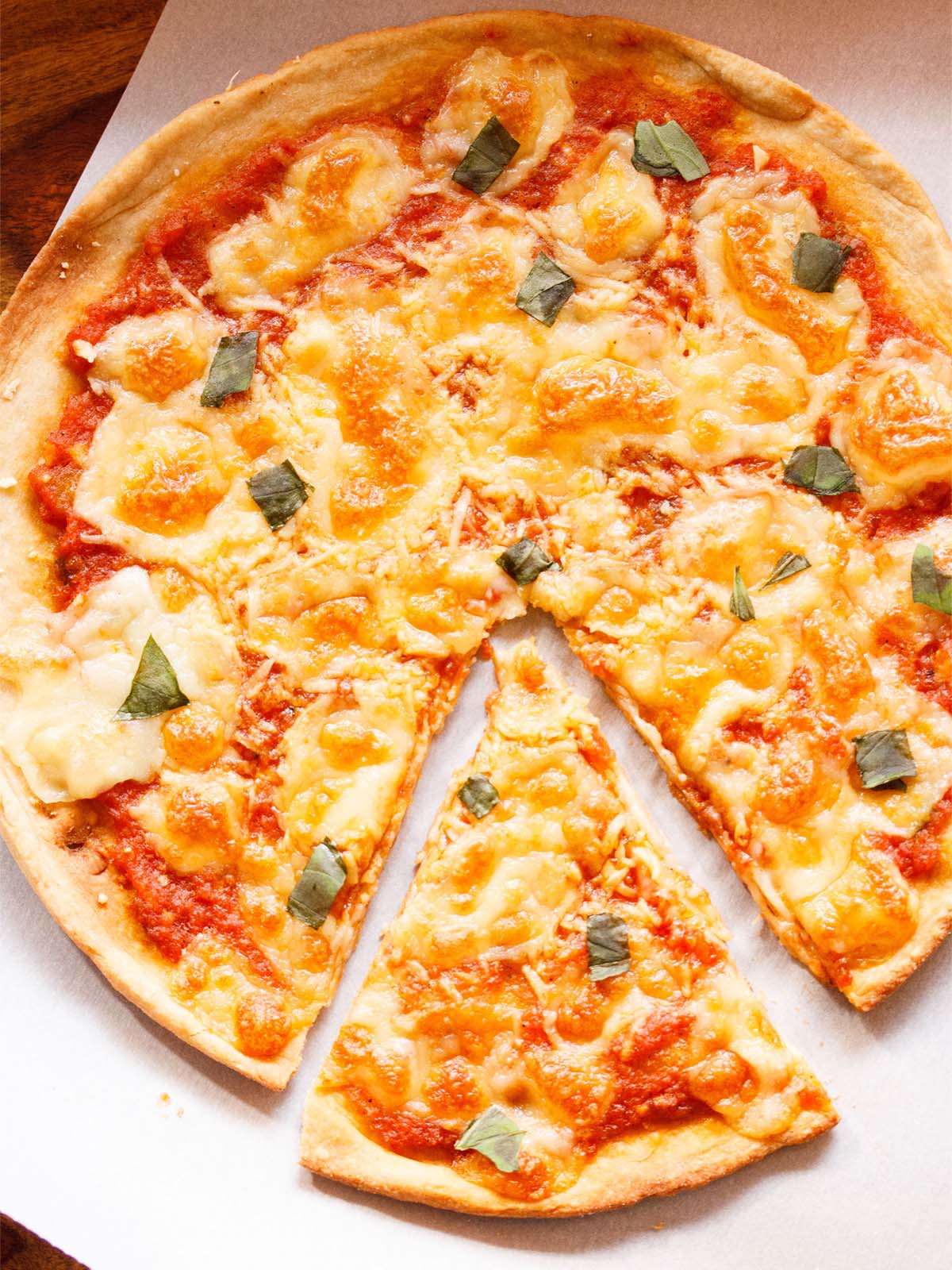 margherita pizza placed on white butter paper with a pizza cutter on top