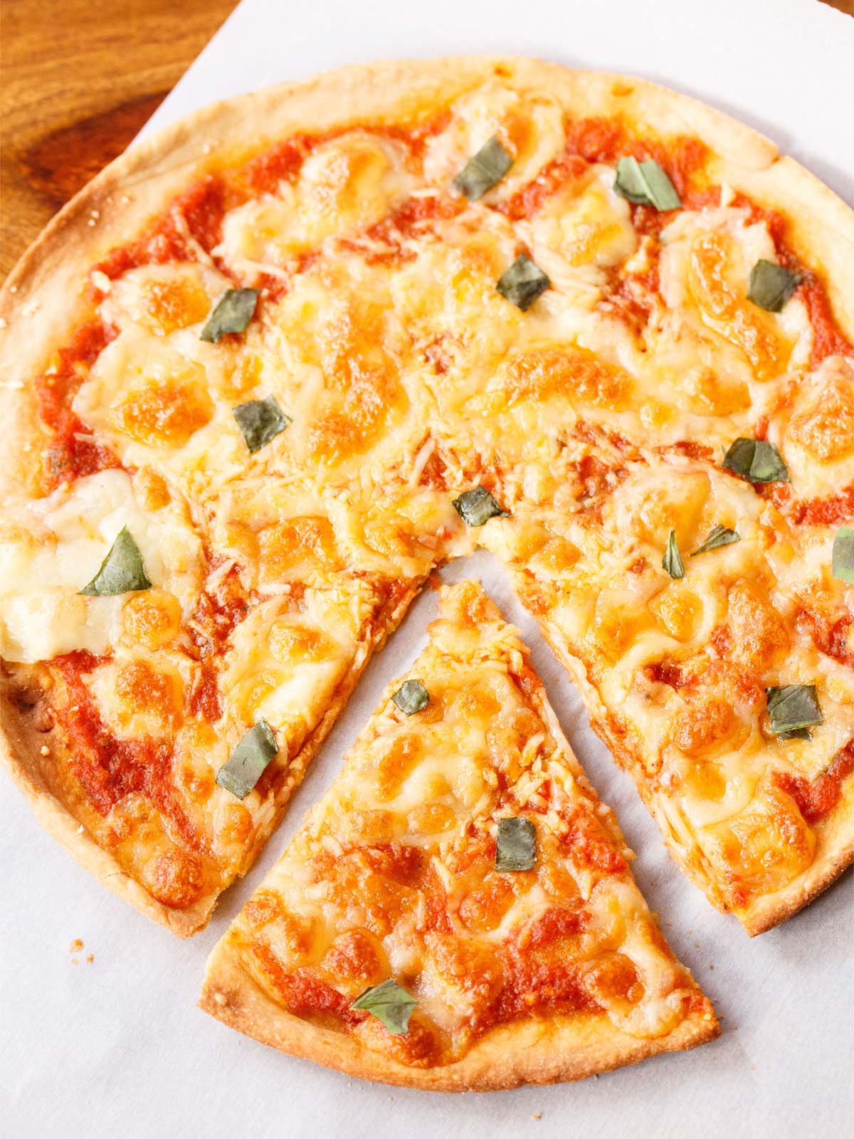 margherita pizza with a wedge separated slightly served on a white butter paper