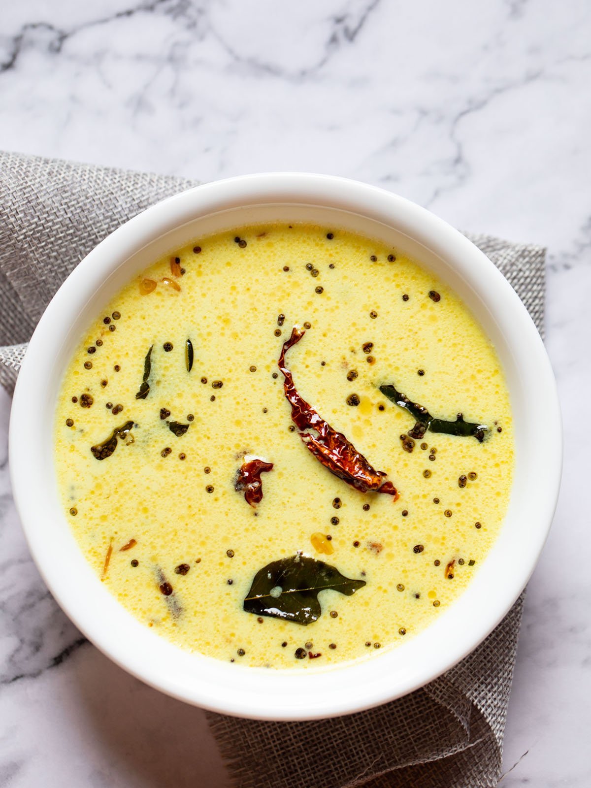 finished bowl of kerala style moru curry or pulissery in a white bowl on a white marble table