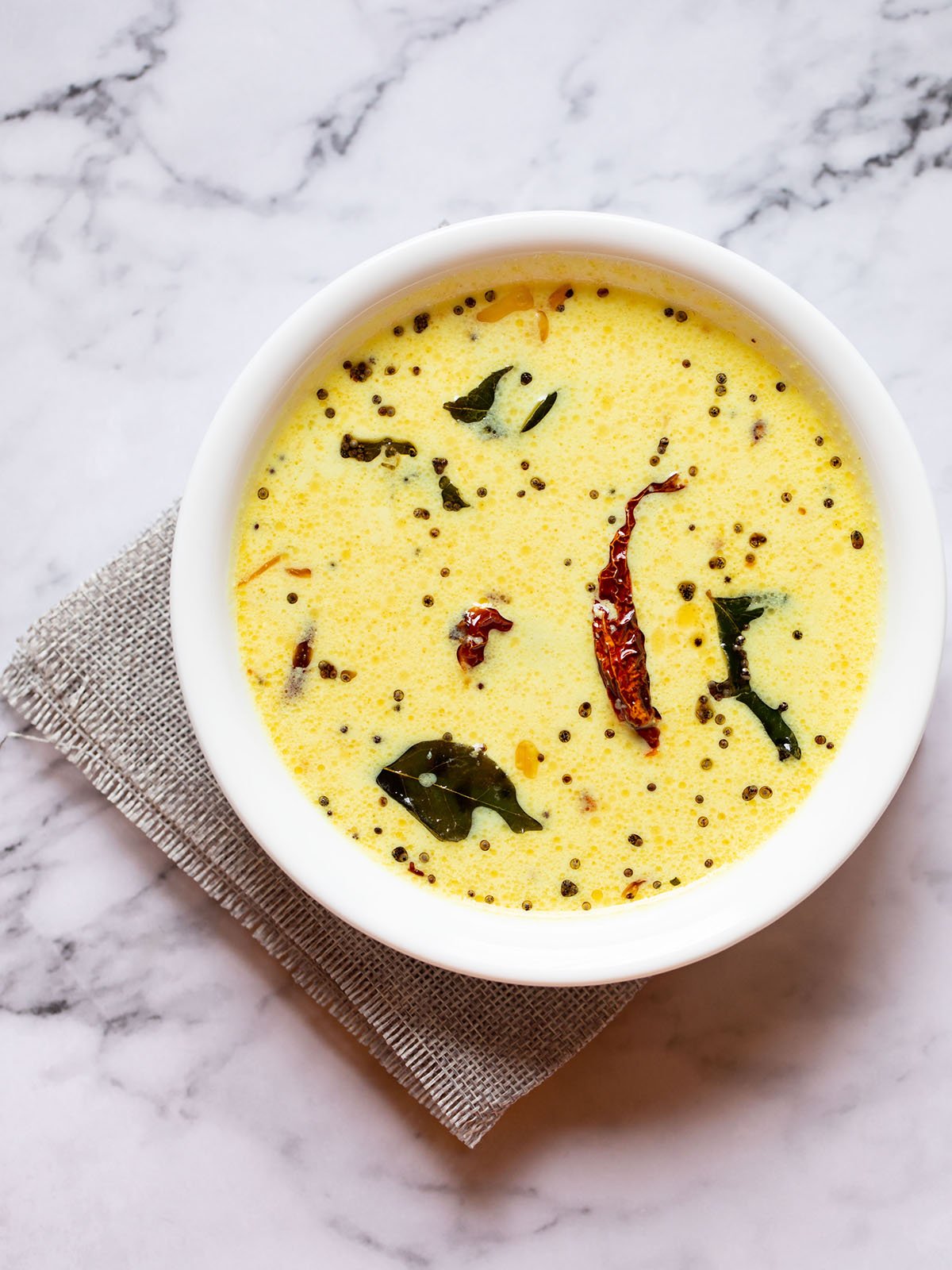 kerala moru curry in a white bowl on a white marble table