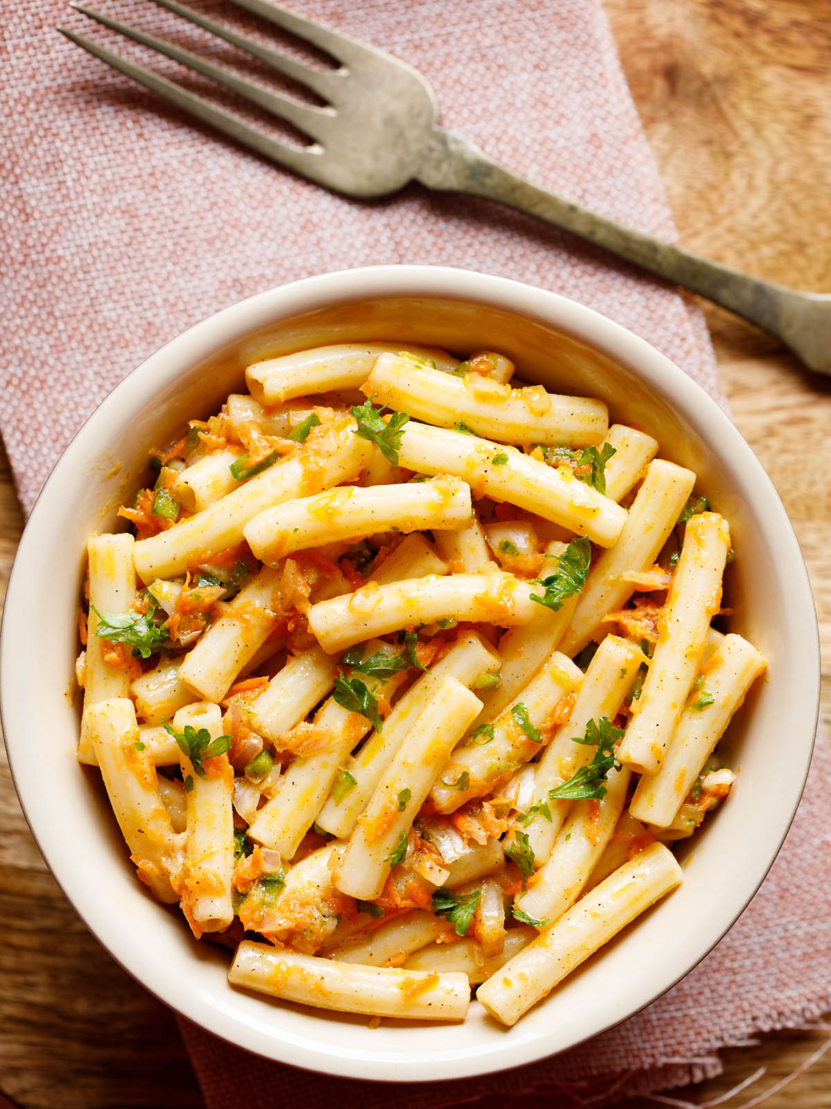 pasta salad in a bowl sprinkled with parsley and a brass fork placed on top