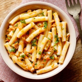 pasta salad in a bowl sprinkled with parsley and a brass fork by side