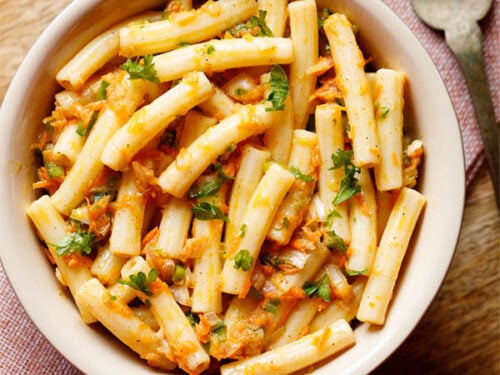pasta salad in a bowl sprinkled with parsley and a brass fork by side