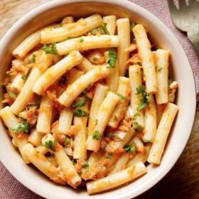 pasta salad in a bowl sprinkled with parsley and a brass fork by side