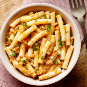 pasta salad in a bowl sprinkled with parsley and a brass fork by side