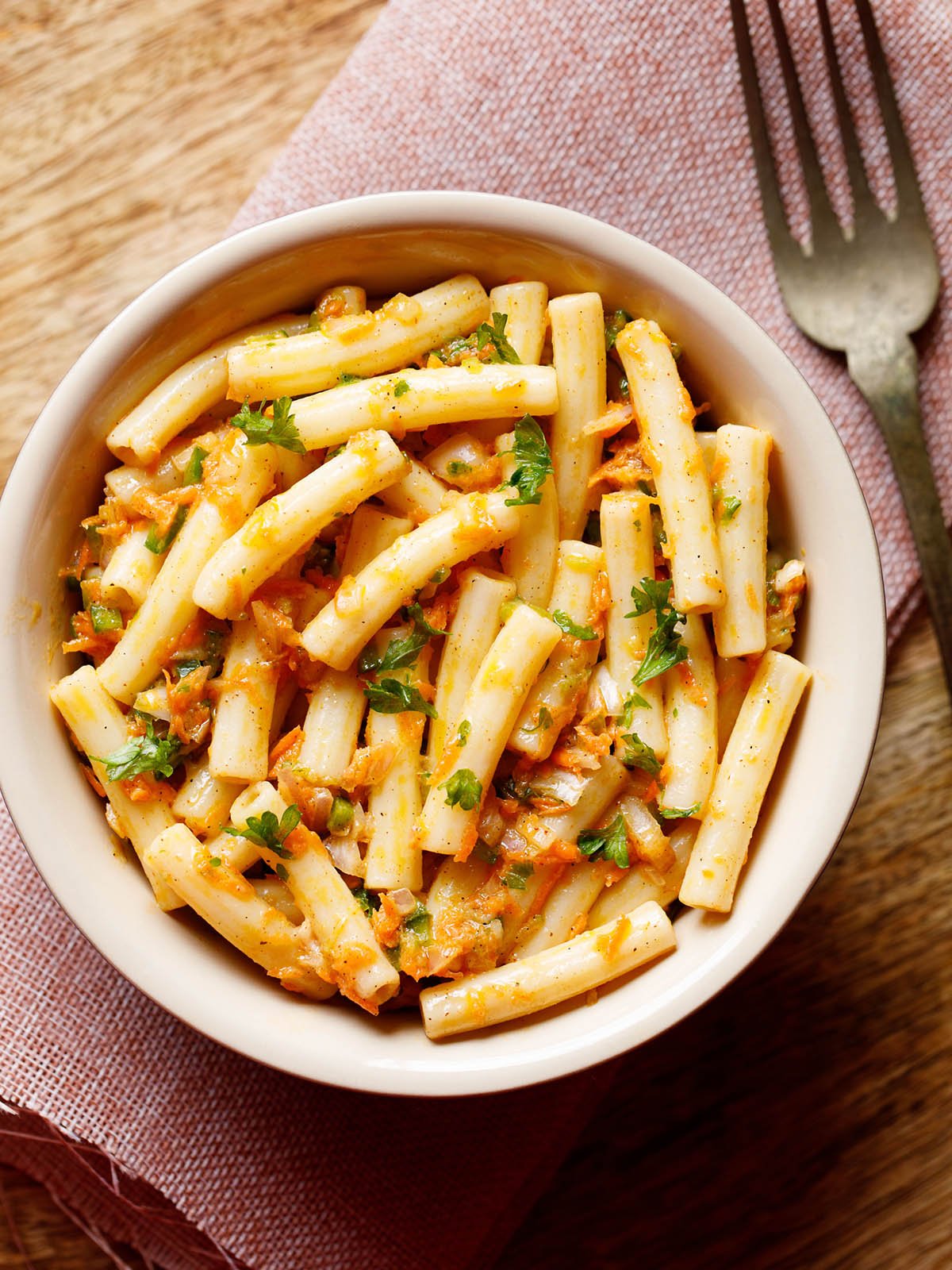 pasta salad in a bowl sprinkled with parsley and a brass fork by side