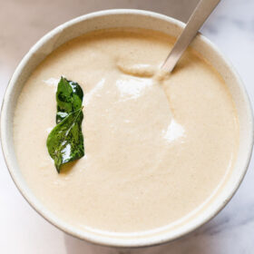 peanut chutney in a ceramic bowl with fried curry leaves on it with a steel spoon