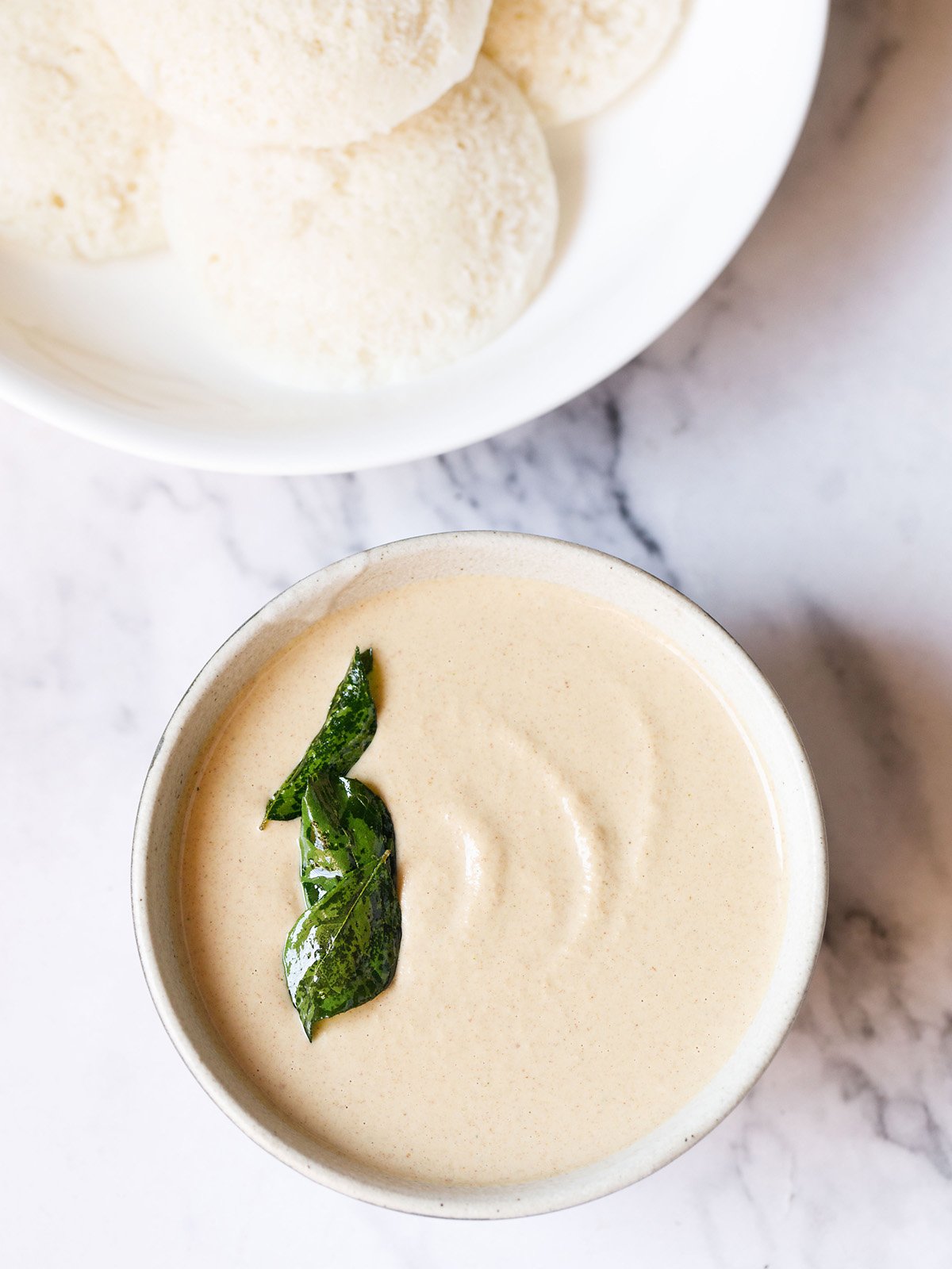 peanut chutney in a ceramic bowl with fried curry leaves on it on a white marble background