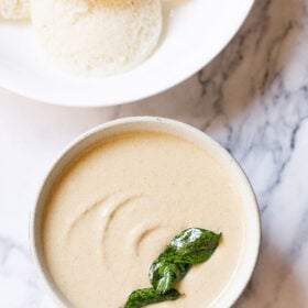 peanut chutney in a ceramic bowl with fried curry leaves on it on a white marble background