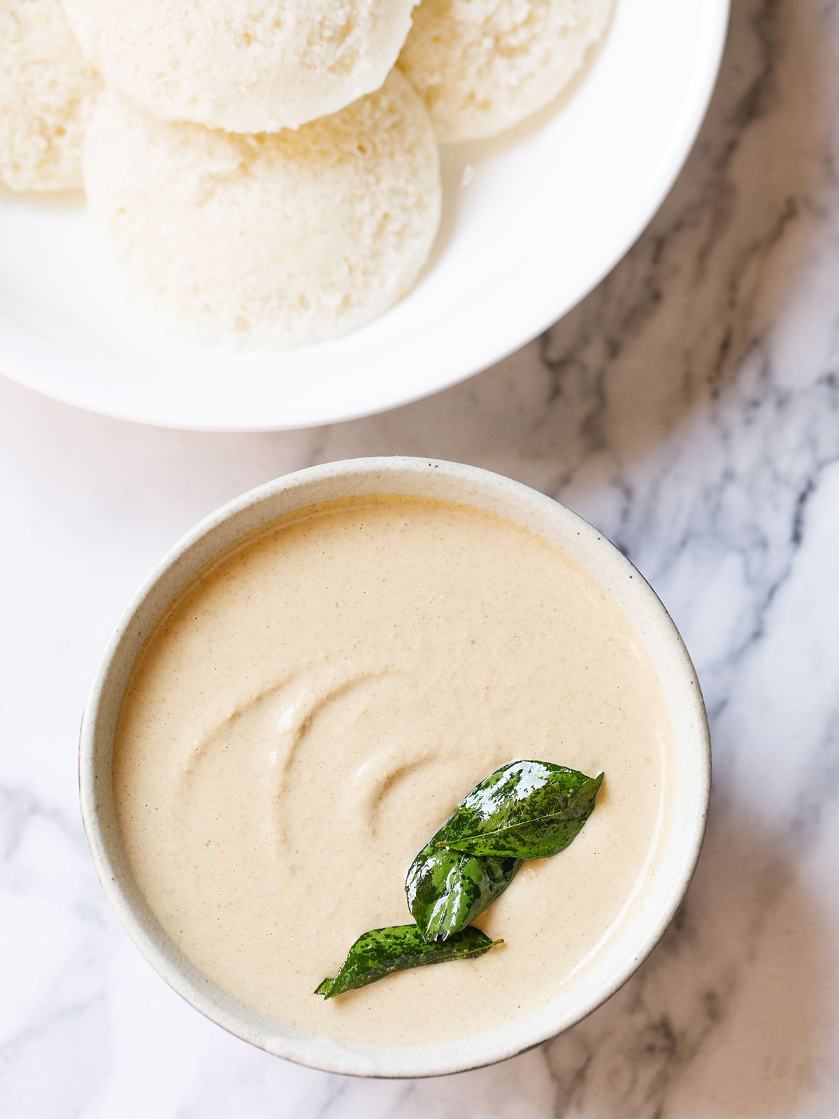 peanut chutney in a ceramic bowl with fried curry leaves on it on a white marble background