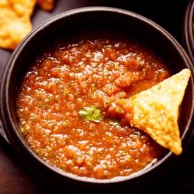 tomato salsa served in a black wooden bowl with a nacho chip dipped in it.