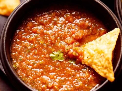 tomato salsa served in a black wooden bowl with a nacho chip dipped in it.