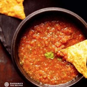 homemade salsa served in a black wooden bowl with a nacho chip dipped in the salsa