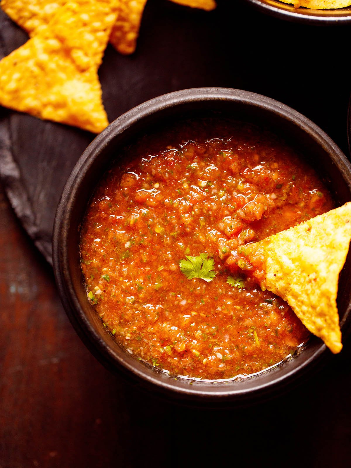 salsa served in a black wooden bowl with a nacho chip dipped in the salsa