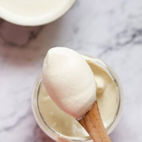 Eggless mayonnaise in a glass jar with a small wooden spoon showing the thickness