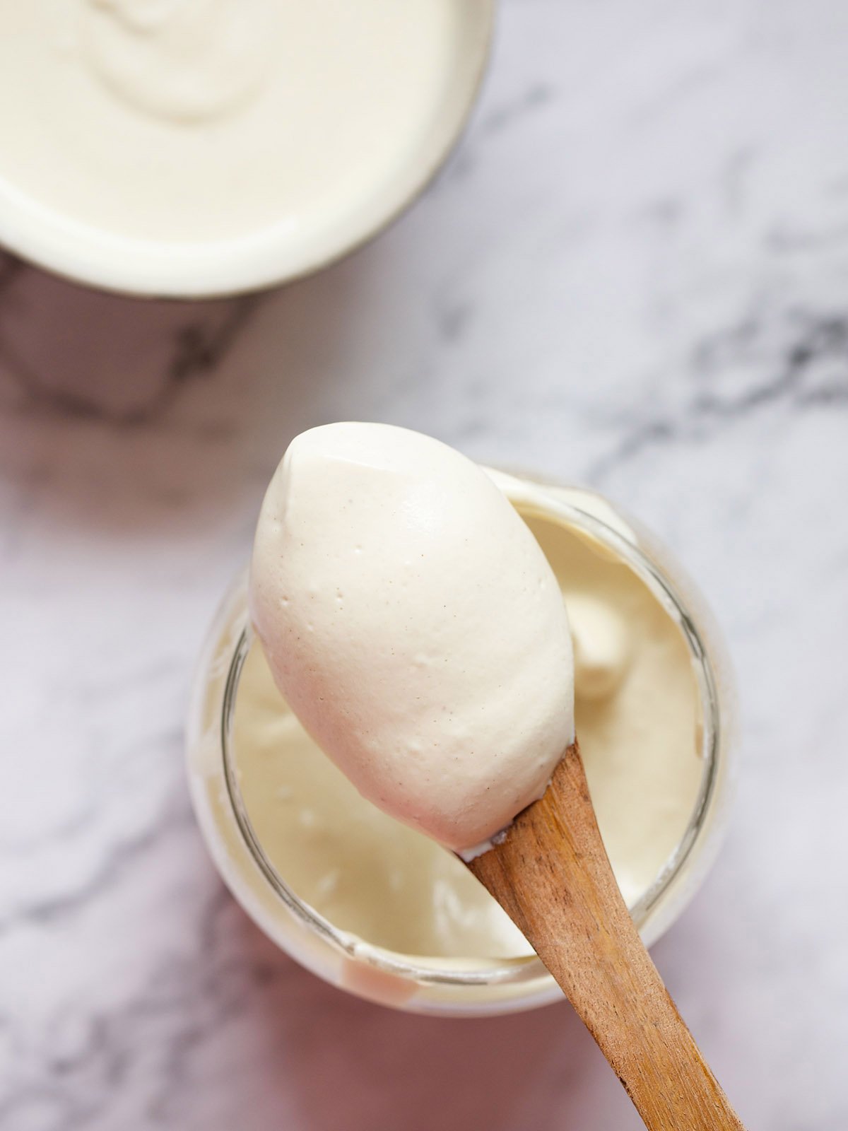 eggless mayonnaise in a glass jar with a small wooden spoon showing the thick consistency