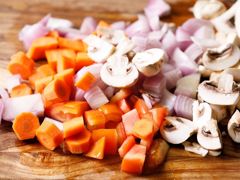 pile of chopped carrots, onions and mushrooms on wooden cutting board