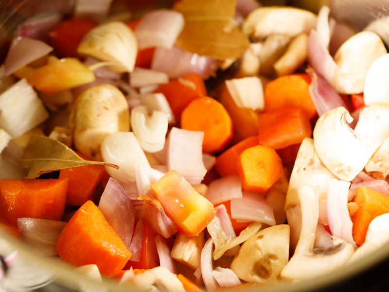 hoja de laurel, cebollas, zanahorias, champiñones y tomates cocinados en una olla