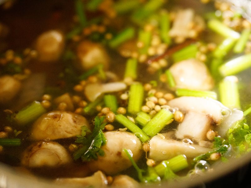 mushrooms, celery and coriander seeds floating in water in stockpot to make vegetable stock