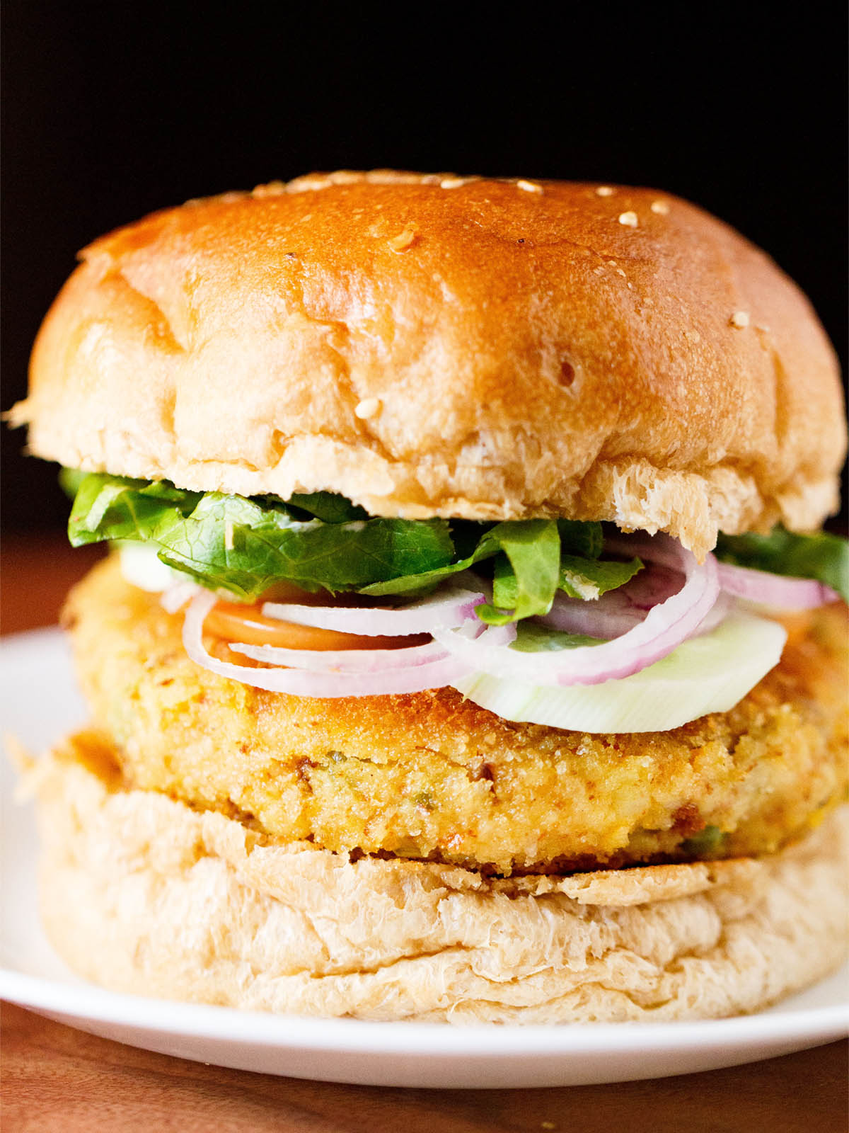 close up photo of burger made with veggie patty, topped with onion, cucumber and lettuce on a white plate