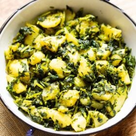 aloo methi in a enameled black rimmed small white wok on a brown jute napkin