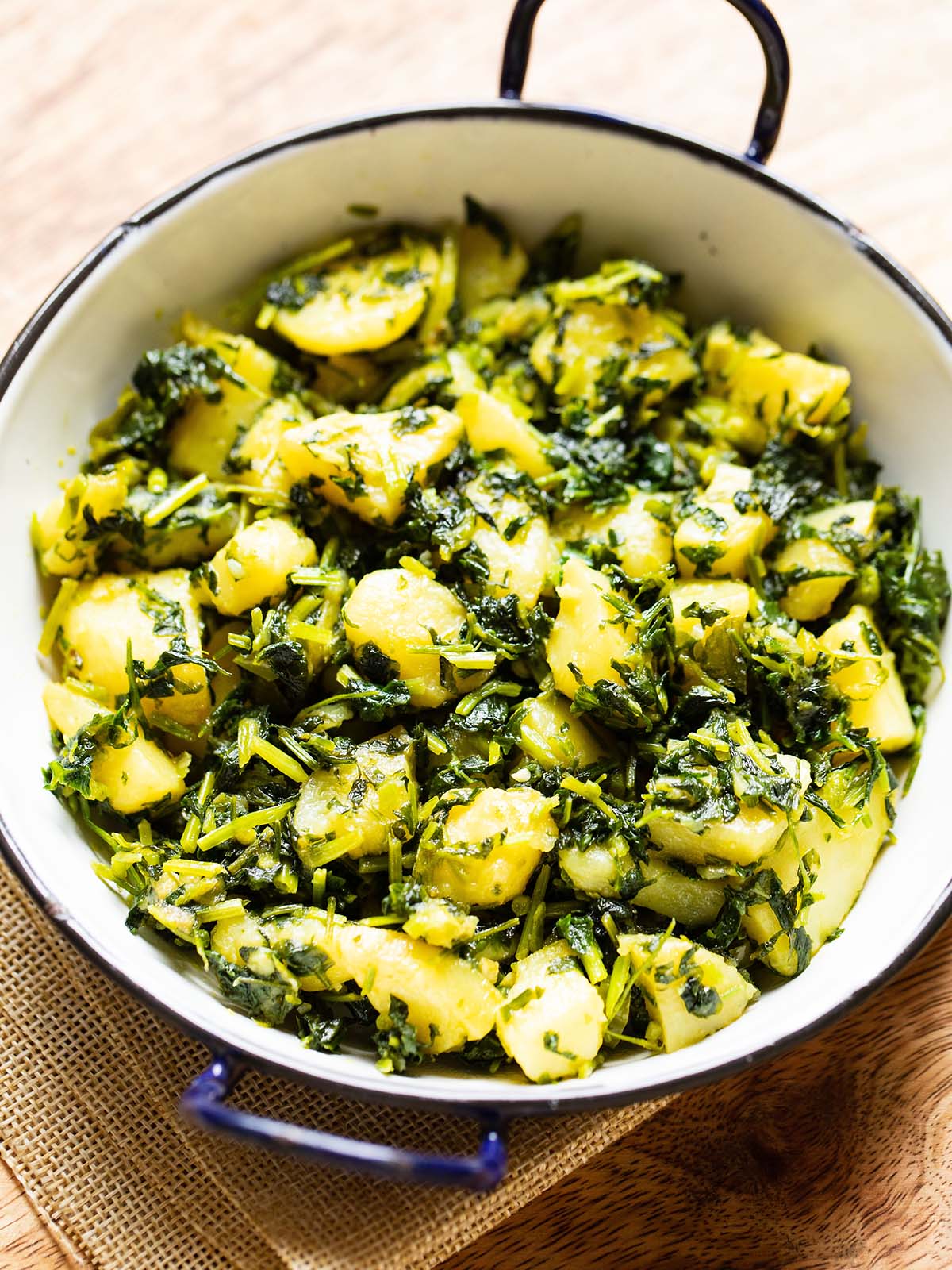 aloo methi in a enameled black rimmed small white wok on a brown jute napkin